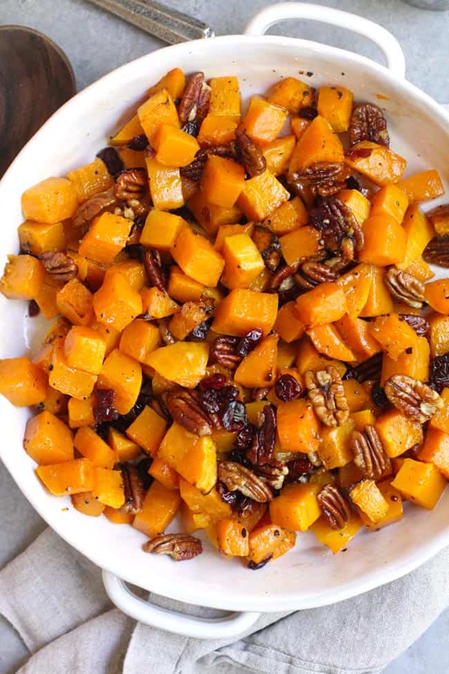 Overhead shot of a white dish of roasted butternut squash with pecans and cranberries.