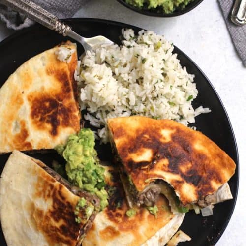 Overhead shot of a plate of steak fajita quesadillas, with a side of guac and a side of cilantro lime rice.