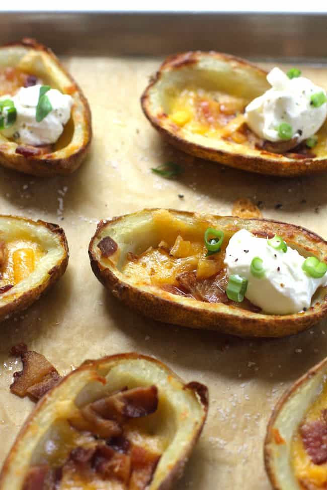 Side shot of several crispy potato skins, loaded with bacon, cheese, and sour cream.