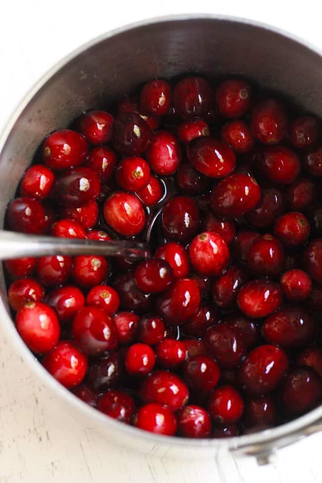 A small saucepan of cranberries soaked in a simple syrup, with a spoon inside.