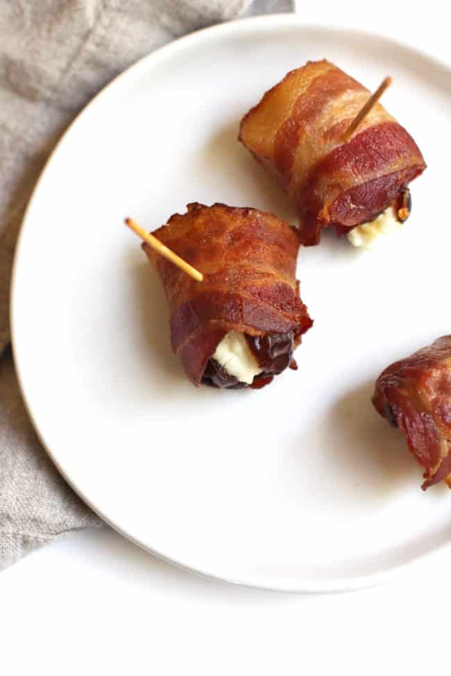 A small white plate with three bacon wrapped dates with goat cheese.