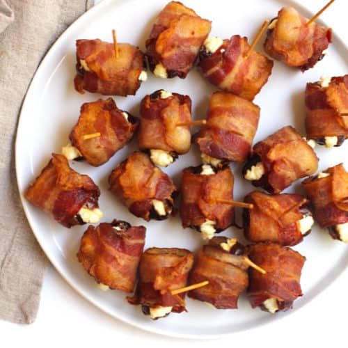A white round plate of bacon wrapped dates with goat cheese, secured with toothpicks.