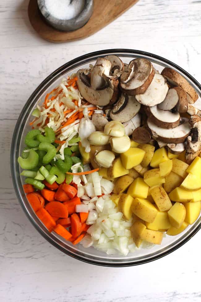 Overhead shot of all the vegetables for the soup, in a large glass bowl, on a white background.