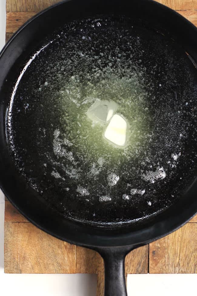 Overhead shot of a cast iron skillet prepared with butter and olive oil.