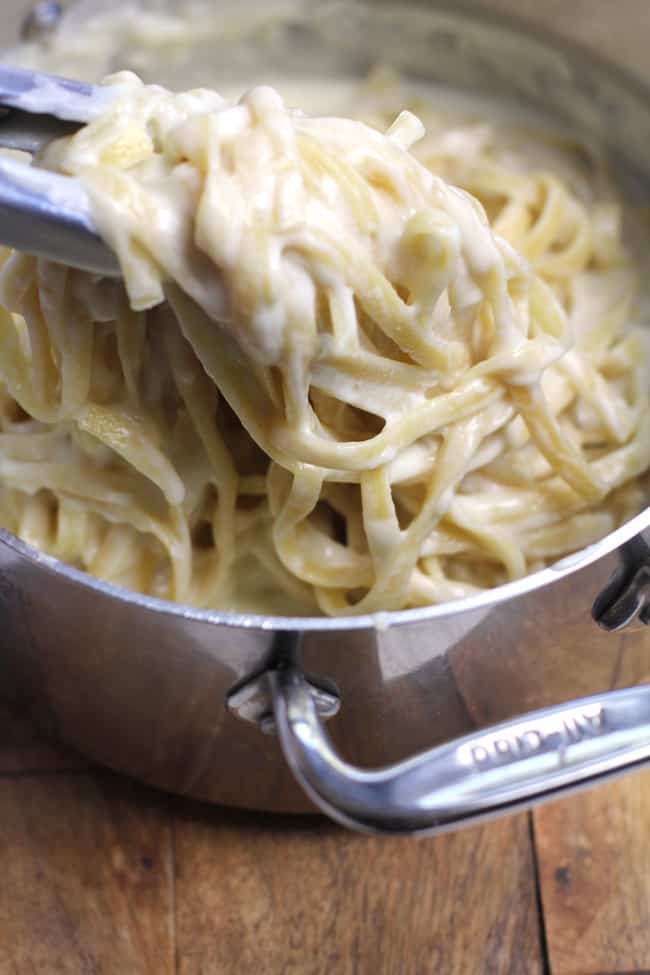 Side shot of a pot of skinny Fettuccini Alfredo, some being lifted up with tongs.