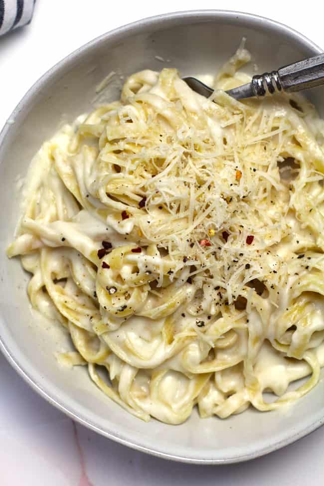 Close up of a bowl of skinny Fettuccini Alfredo, with shaved parmesan and black pepper on top.