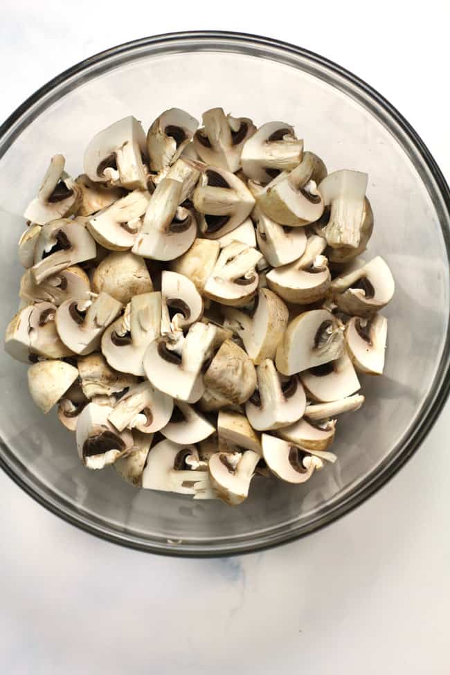 Overhead shot of a glass bowl filled with quartered mushrooms.