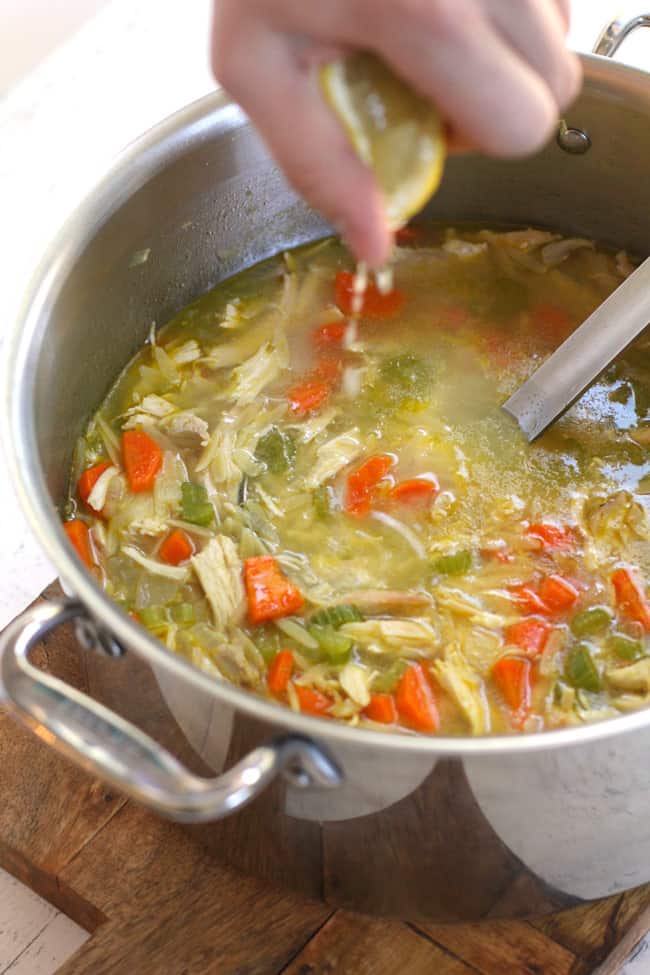 A hand squeezing lemon into a pot of chicken orzo soup.