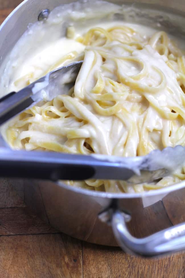 Side shot of a pan of skinny Fettuccini Alfredo, with a tongs inside the pan.