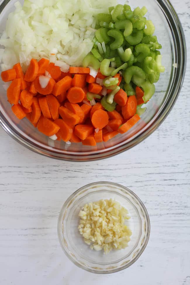 Overhead shot of a glass bowl with chopped celery, carrots, and onion plus a small bowl of minced garlic.