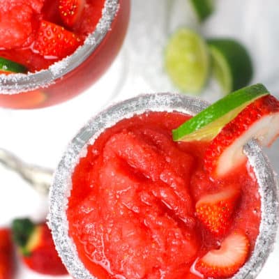 Overhead shot of two frozen strawberry lemonade margaritas, with a salt rim, and lime and strawberry wedges on the glass.
