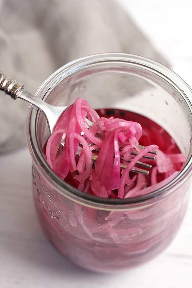 Overhead shot of a forkful of pickled red onions over a jar.