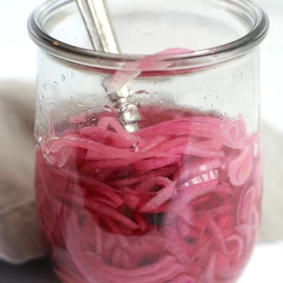 Side view of a jar of quick pickled red onions, with a fork inside the jar.