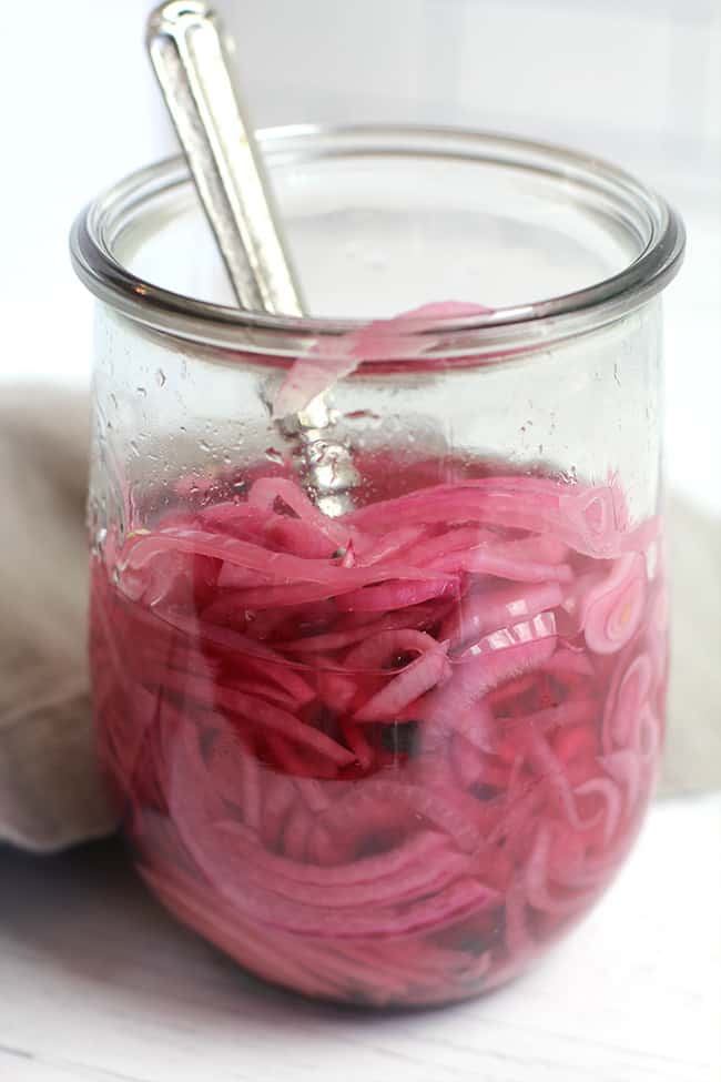 Side view of a jar of quick pickled red onions, with a fork inside the jar.