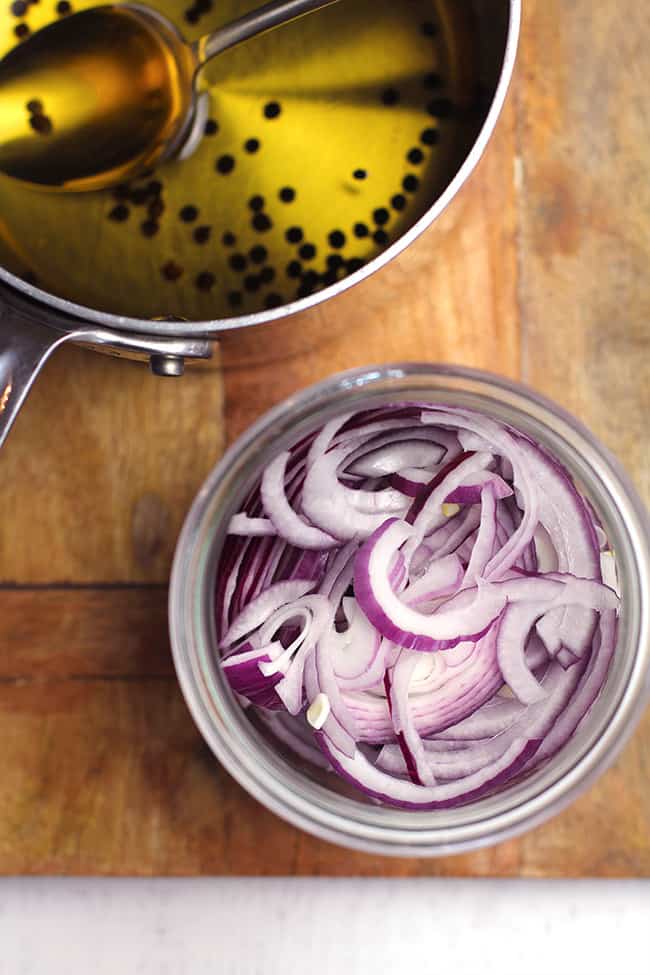 Overhead shot of a jar of sliced red onions and a pan of the pickling ingredients.