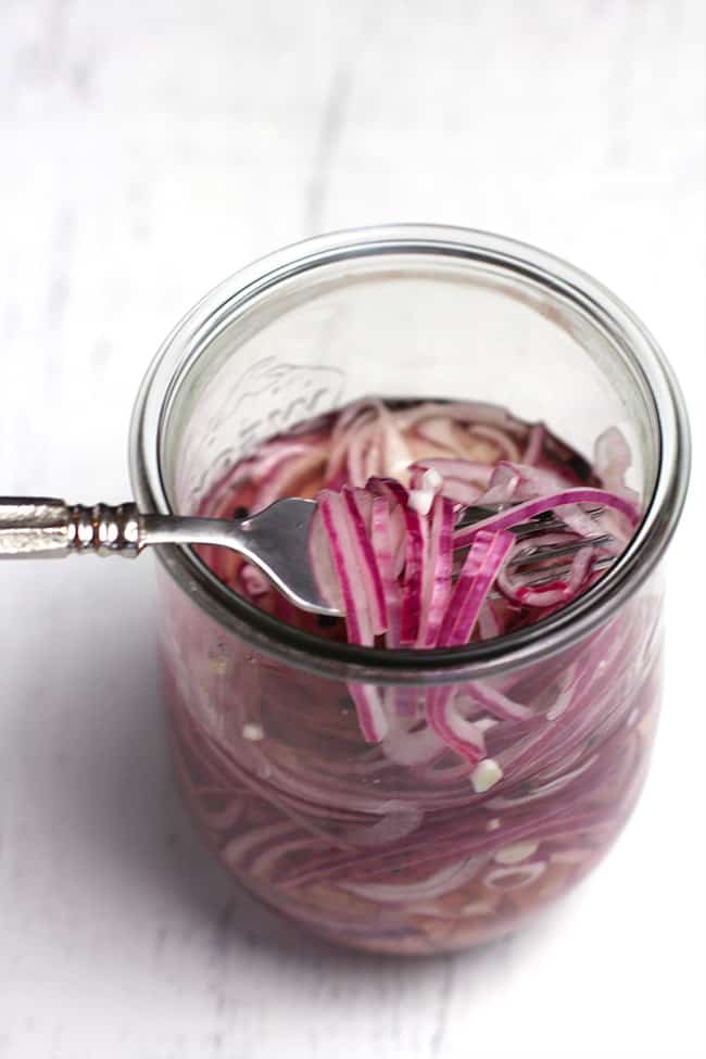 Overhead shot of a jar of pickled onions, with a forkful lifted out, before marinating.