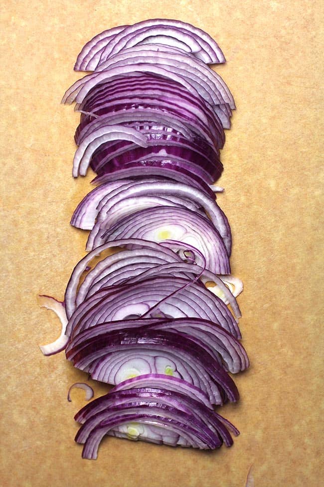Overhead shot of thinly sliced red onion on a cutting board.