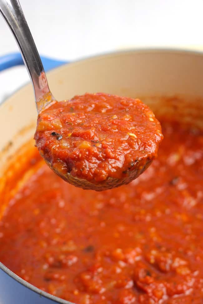 Side shot of a ladle full of homemade marinara sauce, over a pot of sauce.