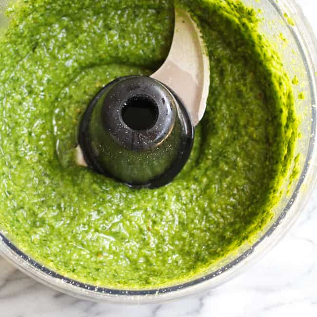 Overhead shot of a food processor filled with pesto sauce.