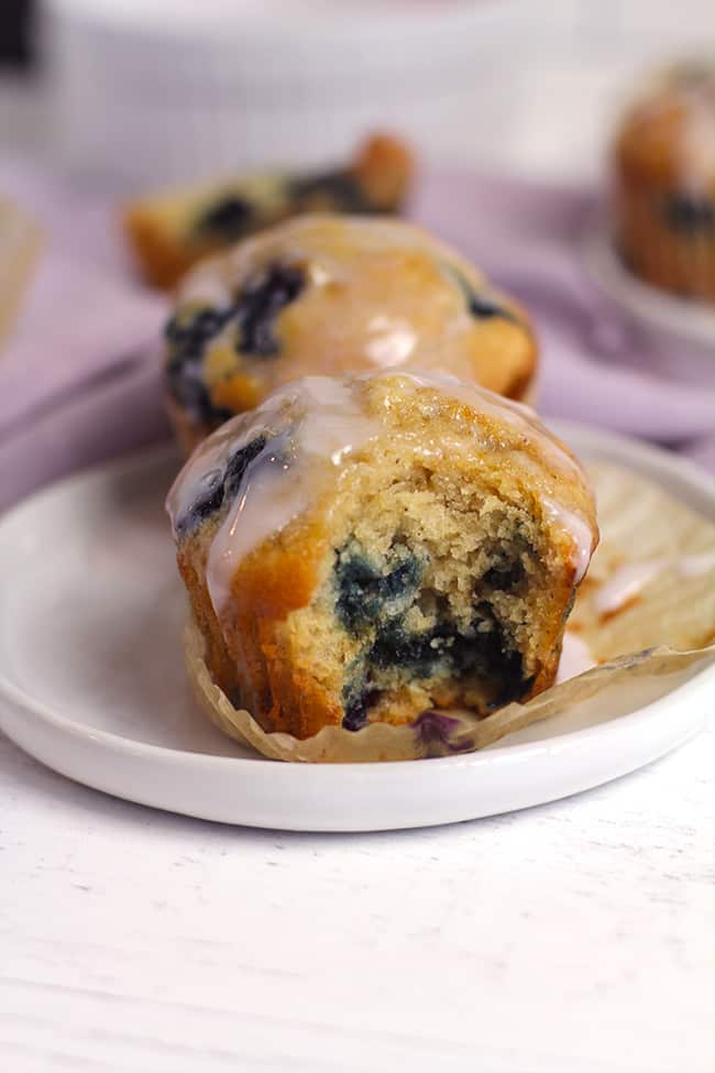 Side shot of a plate of blueberry muffins with a yogurt glaze, and a big bite out of the one in view.