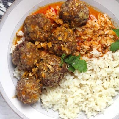 Overhead shot of a gray and white bowl of curried meatballs and rice, on a white background.