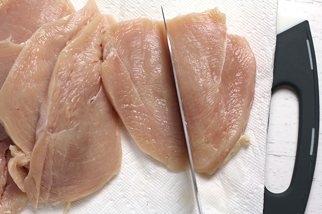 Overhead shot of a cutting board with butterflied and cut chicken breasts.