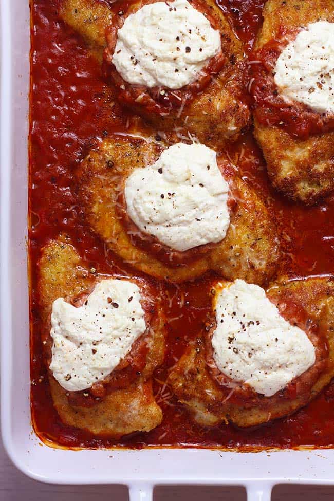 Overhead shot of a white baking dish of Baked Chicken Parmesan, with marinara sauce and ricotta cheese on top.