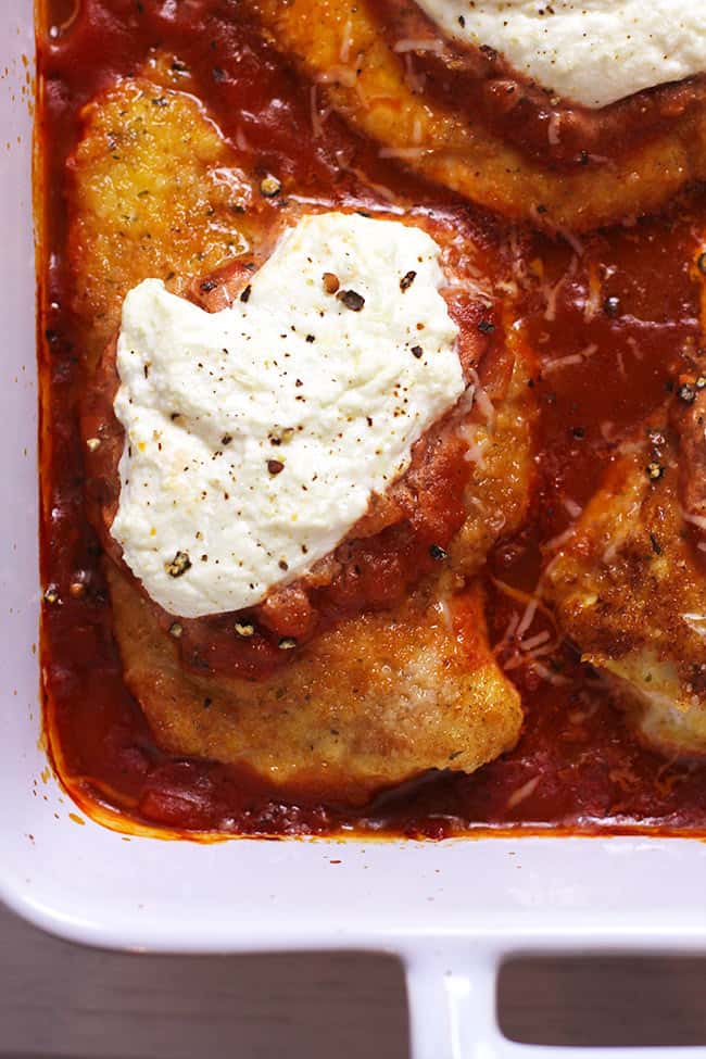 Close up of a piece of Chicken Parm in a casserole dish, with marinara and ricotta cheese.