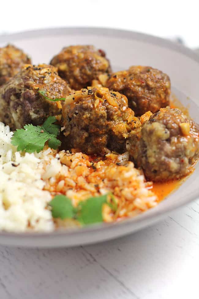 Side shot of a bowl of curried meatballs and rice.