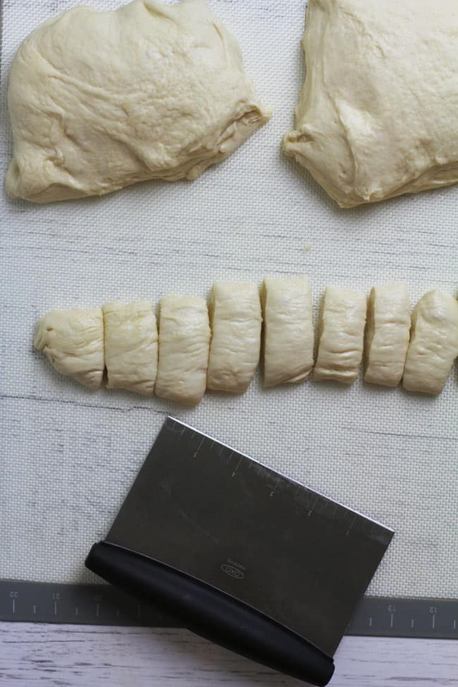 Overhead shot of the dough being cut into bites for boiling, on a baking mat.