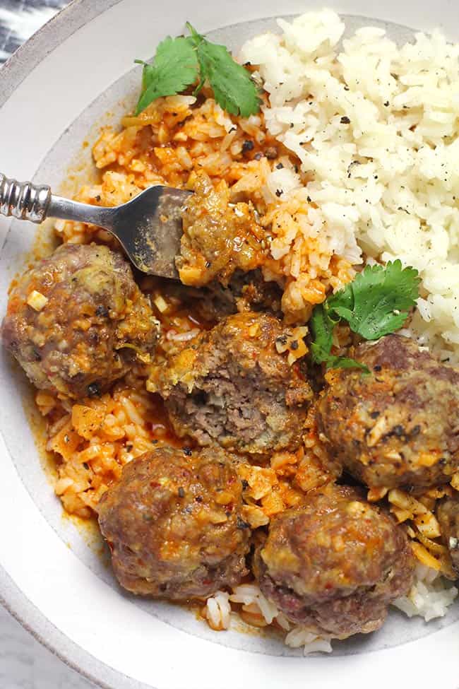 Closeup shot of a bowl of curried meatballs and rice, with a forkful of meatball.