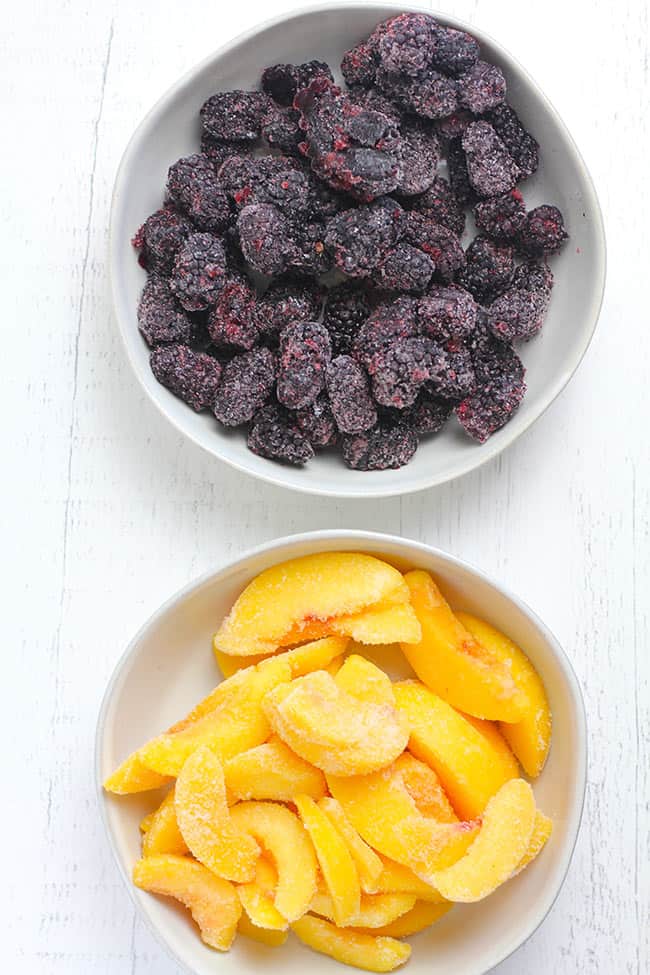 Two white bowls of frozen fruit - one with blackberries and one with peaches.