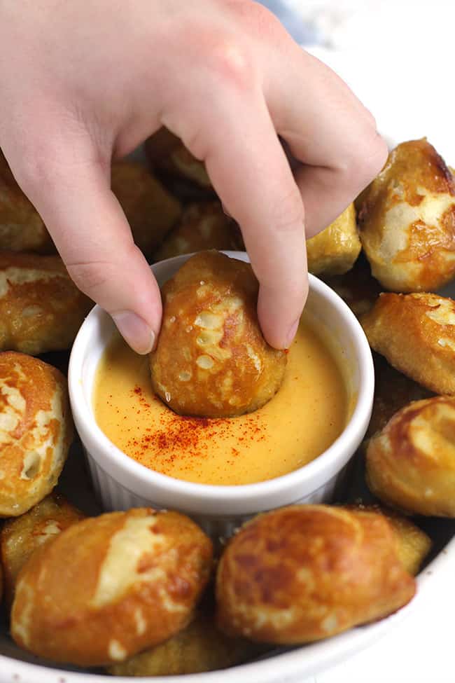 Side shot of a hand dipping a pretzel bite in some cheese dip.