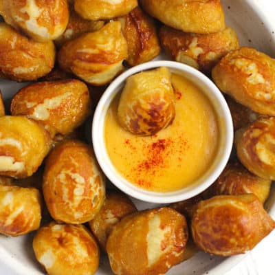 Overhead shot of a white bowl of homemade pretzel bites, with a small bowl of cheese dip in the middle holding one pretzel bite.