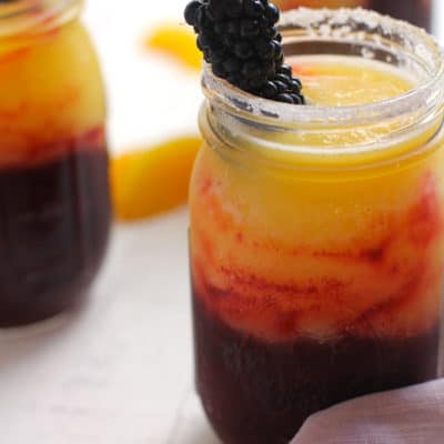 Side shot of blackberry peach frozen margaritas, on a white background with a purple napkin.