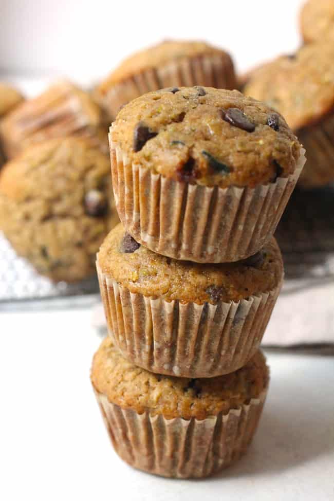 Side shot of a stack of three chocolate chip zucchini muffins, with other muffins in the background.