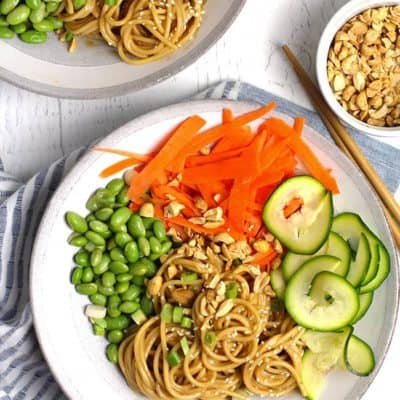 Overhead shot of two bowls of peanut sesame noodles with vegetables, on a white background.