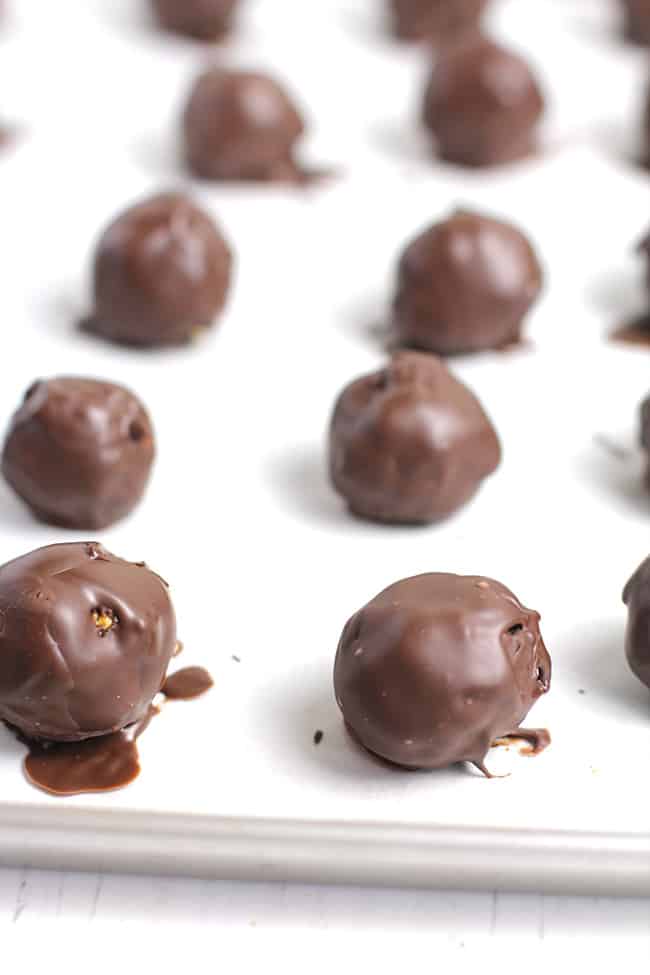 Side shot of a baking sheet of just made dark chocolate covered energy bites.