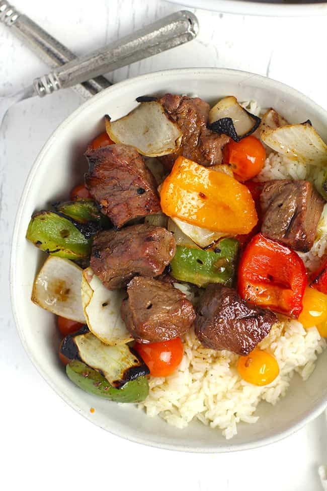 Overhead shot of a white bowl of steak kabobs, bell peppers, and onions, over rice.