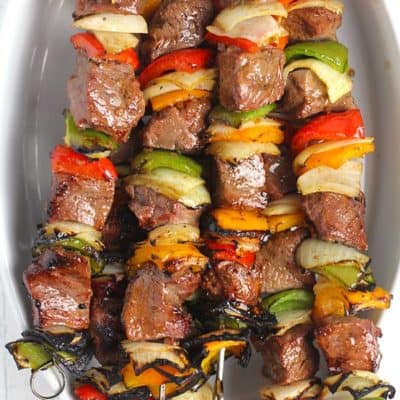 Overhead shot of an oblong white dish, with a bunch of grilled steak kabobs inside.