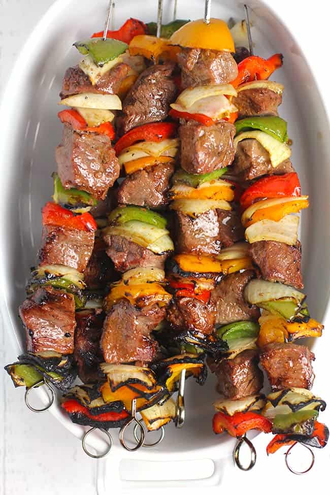 Overhead shot of an oblong white dish, with a bunch of grilled steak kabobs inside.