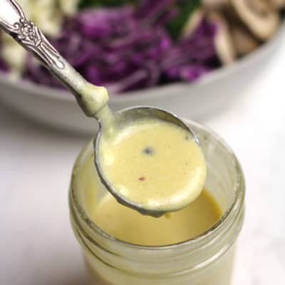 A measuring tablespoon lifted out of a mason jar of dressing, showing the consistency of the honey mustard dressing.