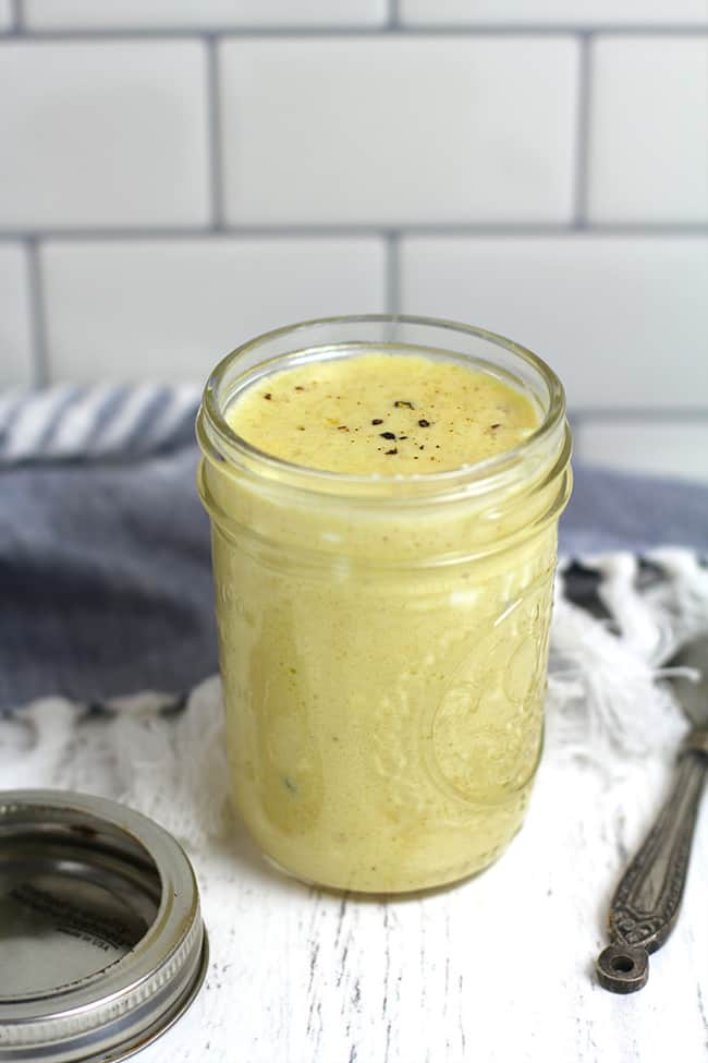 Side shot of a mason jar full of light honey mustard dressing, against a white background.