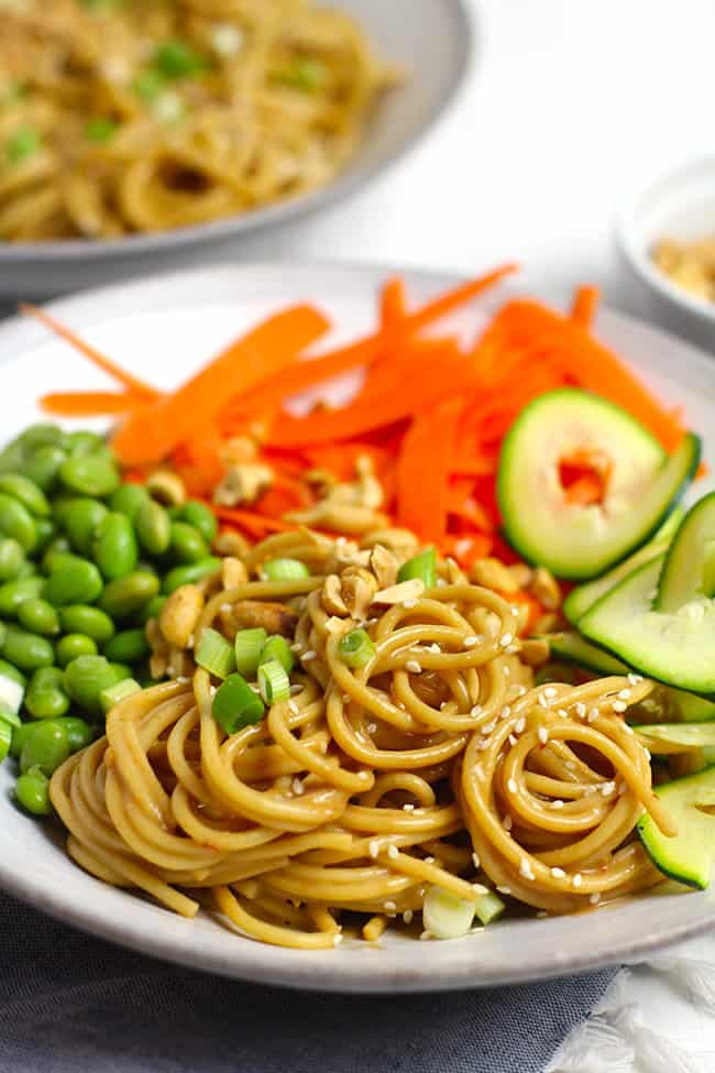Side shot of a bowl of peanut sesame noodles, with vegetables.