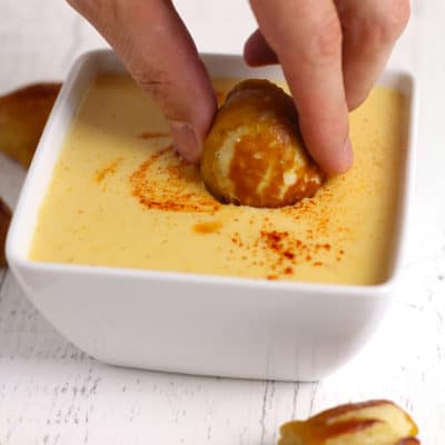A hand dipping a pretzel dip in the cheese dip.
