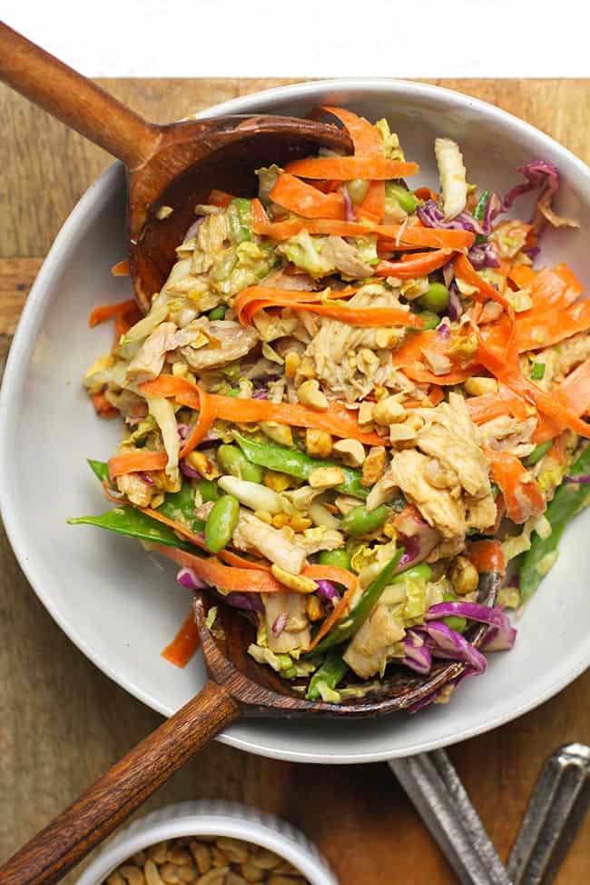 Overhead shot of a white serving bowl of crunchy Thai chicken salad with peanut dressing, with two wooden spoons.