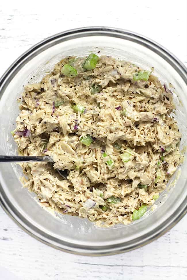 Overhead shot of a clear bowl of the finished tuna salad, with a spoon inside.