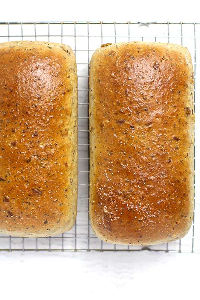 Overhead shot of two loafs of multi-grain-seeded bread on a cooling rack.