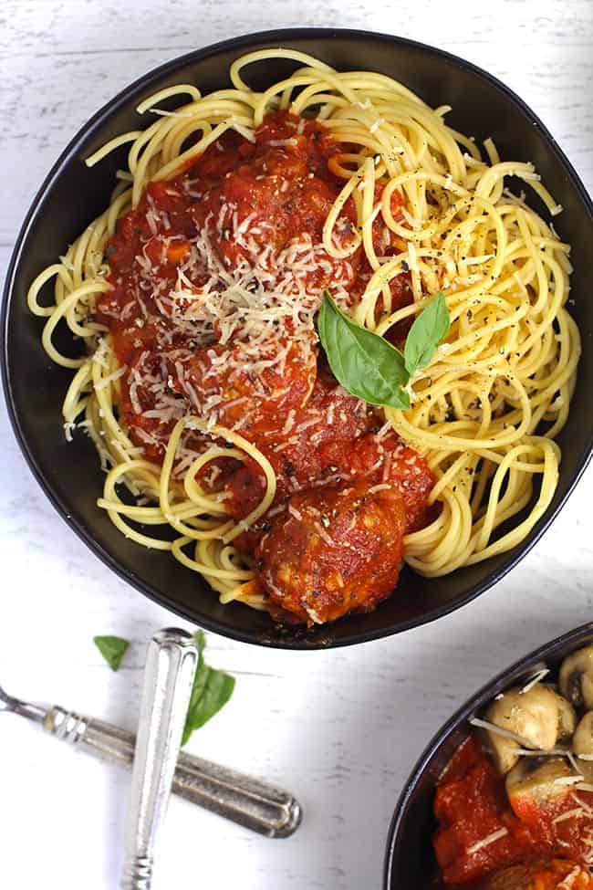 Overhead shot of a black bowl of homemade spaghetti and meatballs, on a white background.