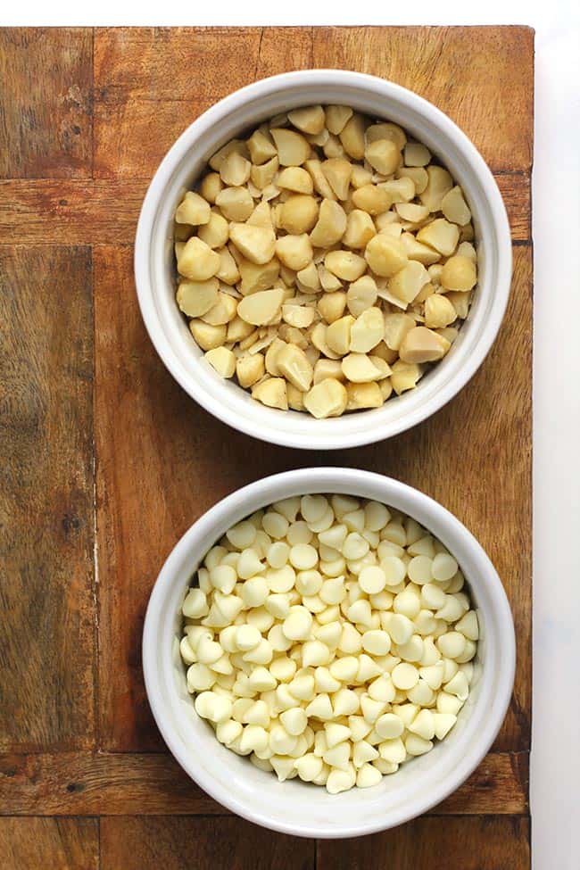 Small bowls of white chocolate chips and chopped macadamia nuts.